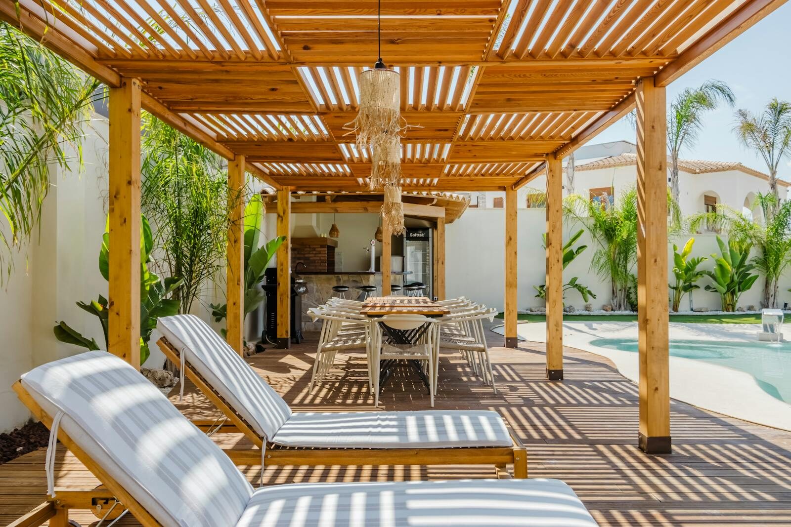 Elegant outdoor patio featuring wooden pergola, chairs, and pool for relaxation under the sun.